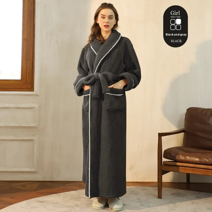 Woman wearing long black and gray fleece bathrobe with white trim, standing indoors near window and chair