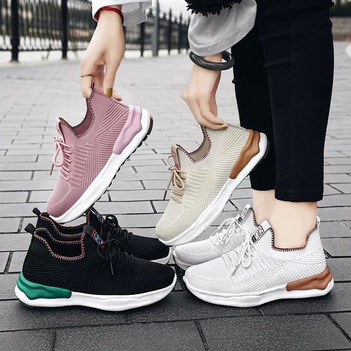 Four pairs of stylish knitted sneakers in pink, beige, black with green, and white with brown soles on tiled pavement