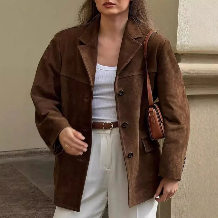Woman wearing a brown suede blazer, white tank top, white pants, and carrying a brown leather shoulder bag