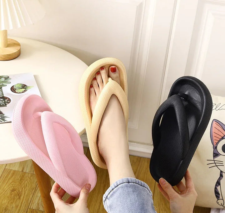 Person wearing beige foam flip-flop sandal holding pink and black foam flip-flops indoors