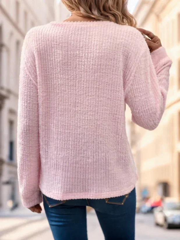 Woman wearing a soft pink textured sweater and blue jeans outdoors in urban setting