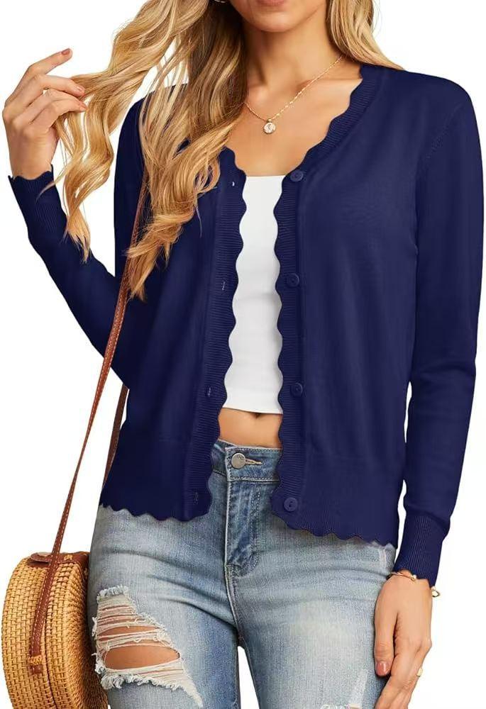 Woman wearing navy blue button-up cardigan with scalloped edges, white crop top, ripped jeans, and carrying a round straw bag