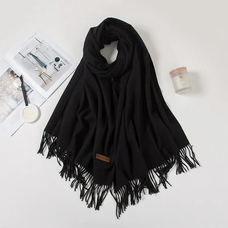 Black fringed scarf laid out on white surface with open magazine and scented candle nearby