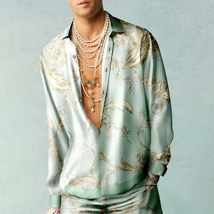 Man wearing satin floral print shirt and multiple layered necklaces on light blue background