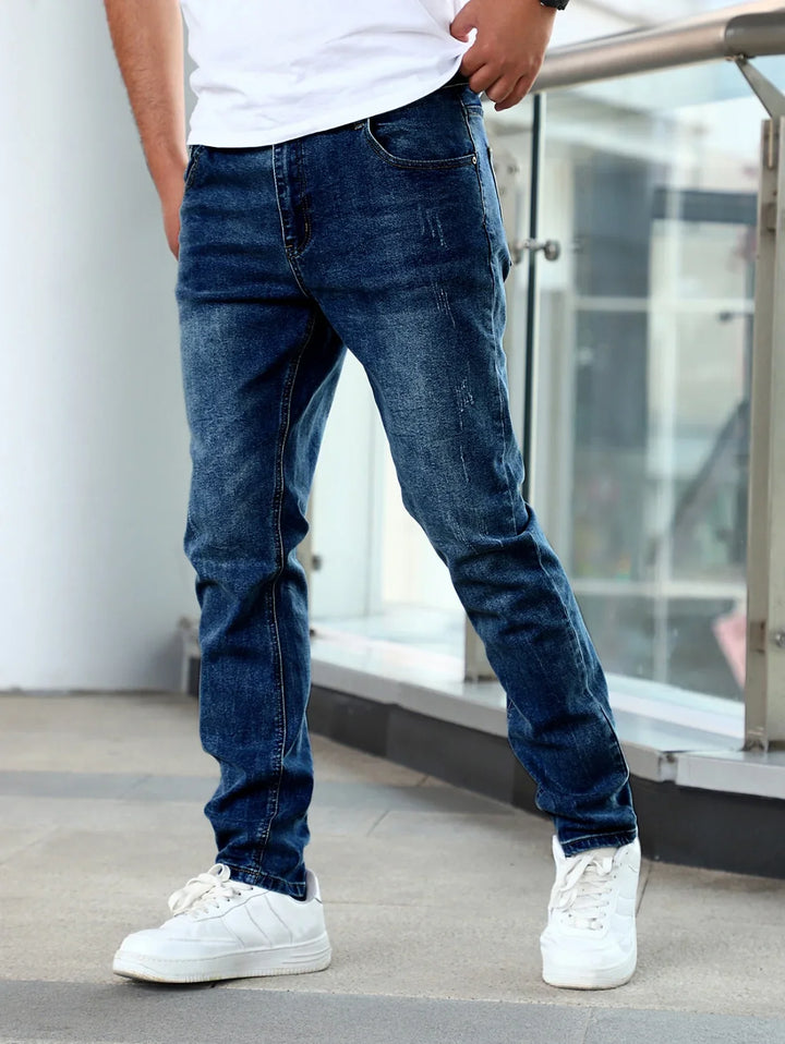 Man wearing slim fit dark blue denim jeans and white sneakers standing indoors