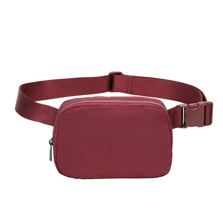 Minimalist burgundy waist bag with zipper and adjustable strap on white background