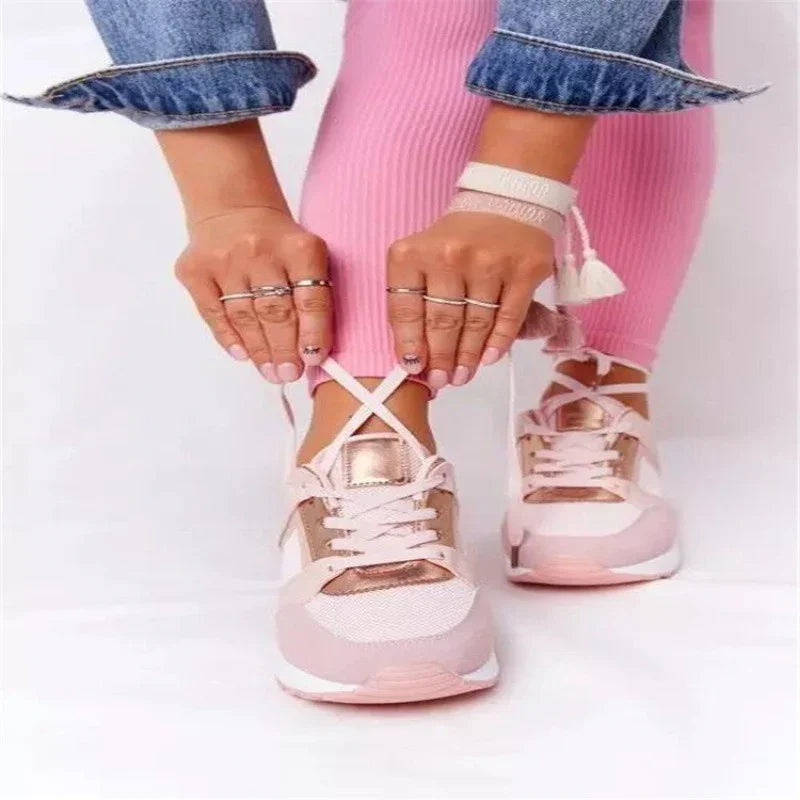 Person tying laces on pink and white sneakers with metallic rose gold accents and pink pants