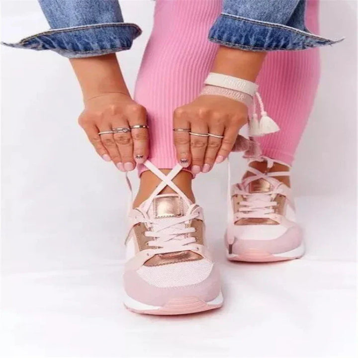 Person tying laces on pink and white sneakers with metallic rose gold accents and pink pants