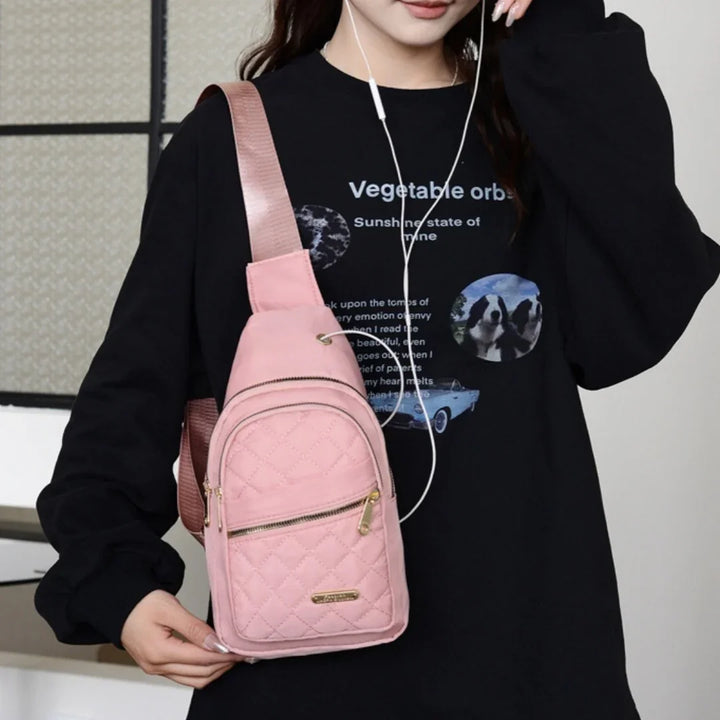 Woman wearing black graphic sweatshirt with earphones and holding pink quilted sling backpack bag