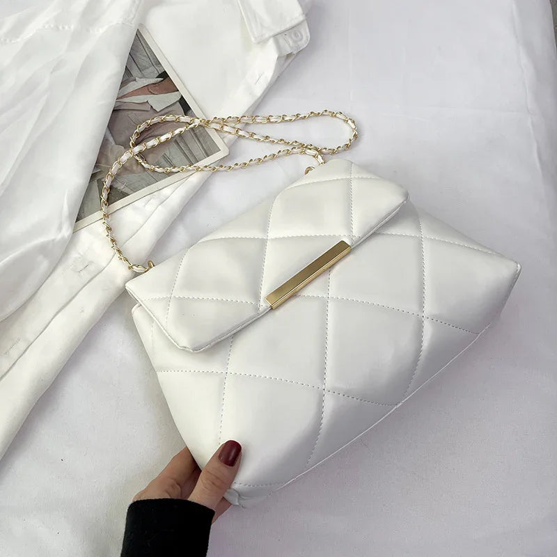 Hand holding white quilted leather handbag with gold chain strap on white fabric background