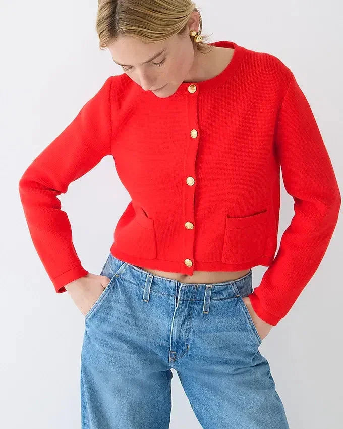 Woman wearing a bright red cardigan with gold buttons and high-waisted blue jeans against white background