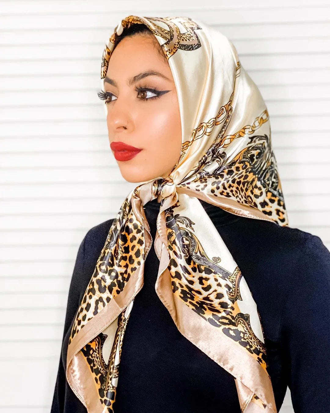 Woman wearing a silky leopard print and chain patterned headscarf with bold red lipstick and winged eyeliner