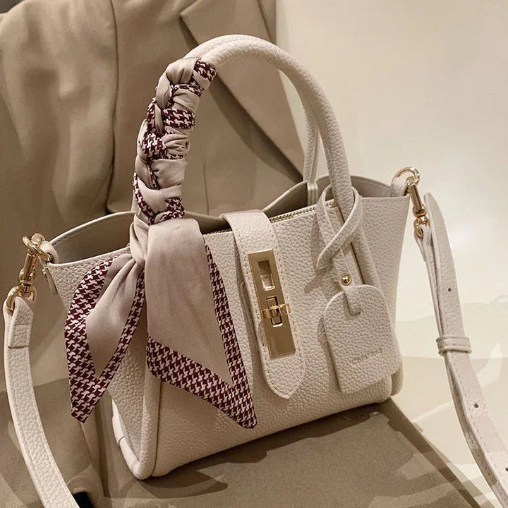 Elegant white textured leather handbag with gold hardware and a beige and maroon patterned scarf on handle