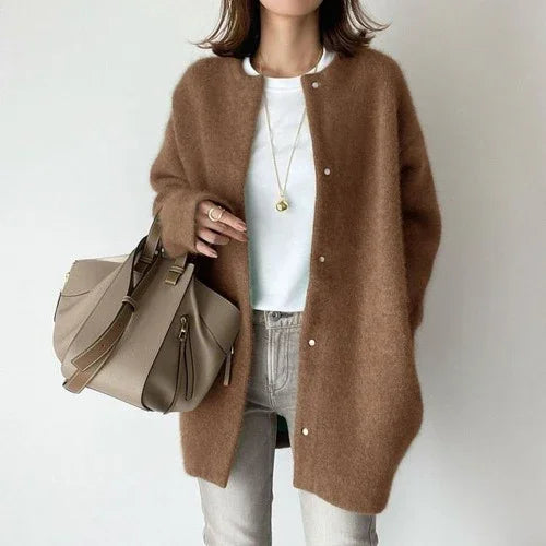 Woman wearing brown fuzzy cardigan, white T-shirt, gray jeans, holding beige handbag with gold chain