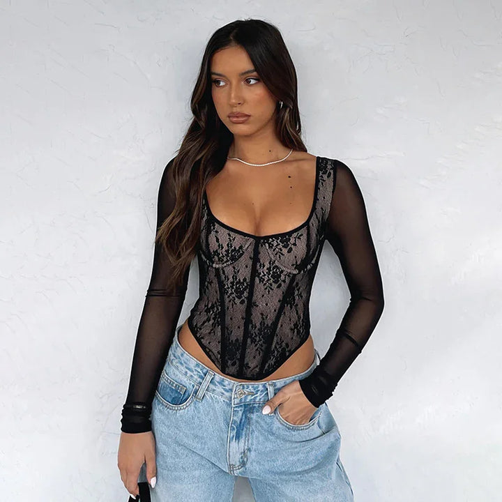 woman wearing black lace bodysuit with sheer long sleeves and light blue jeans against white wall