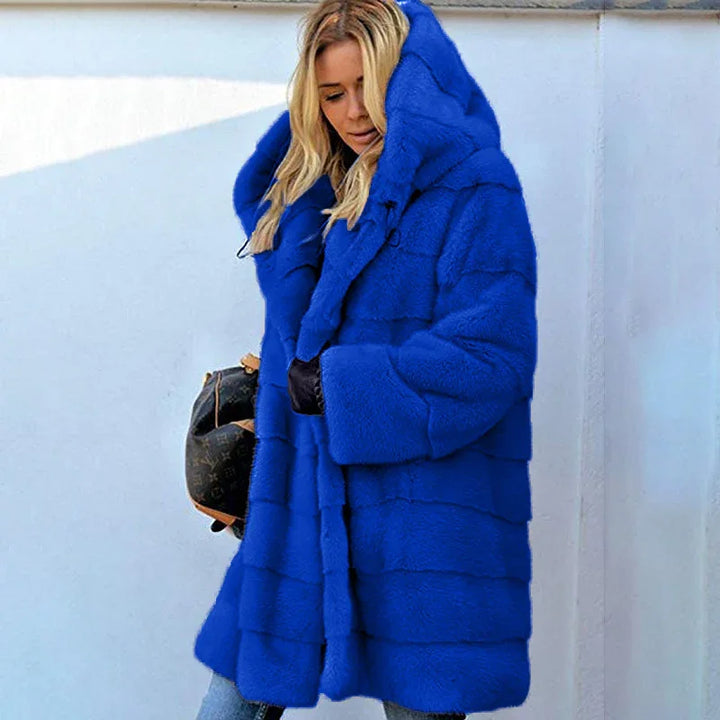 Woman wearing vibrant blue oversized faux fur coat with large hood holding a handbag