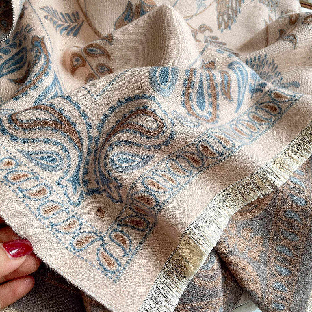Close-up of beige and blue paisley patterned fabric with fringed edge held by hand with red nail polish