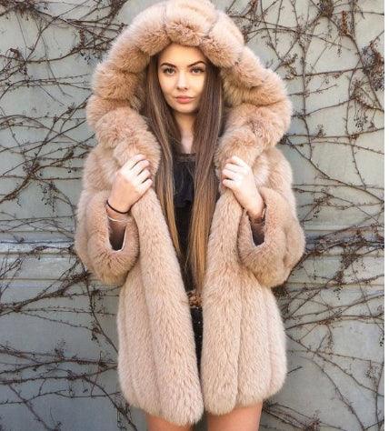 Young woman wearing beige faux fur coat with hood, standing against a wall with dried vine branches