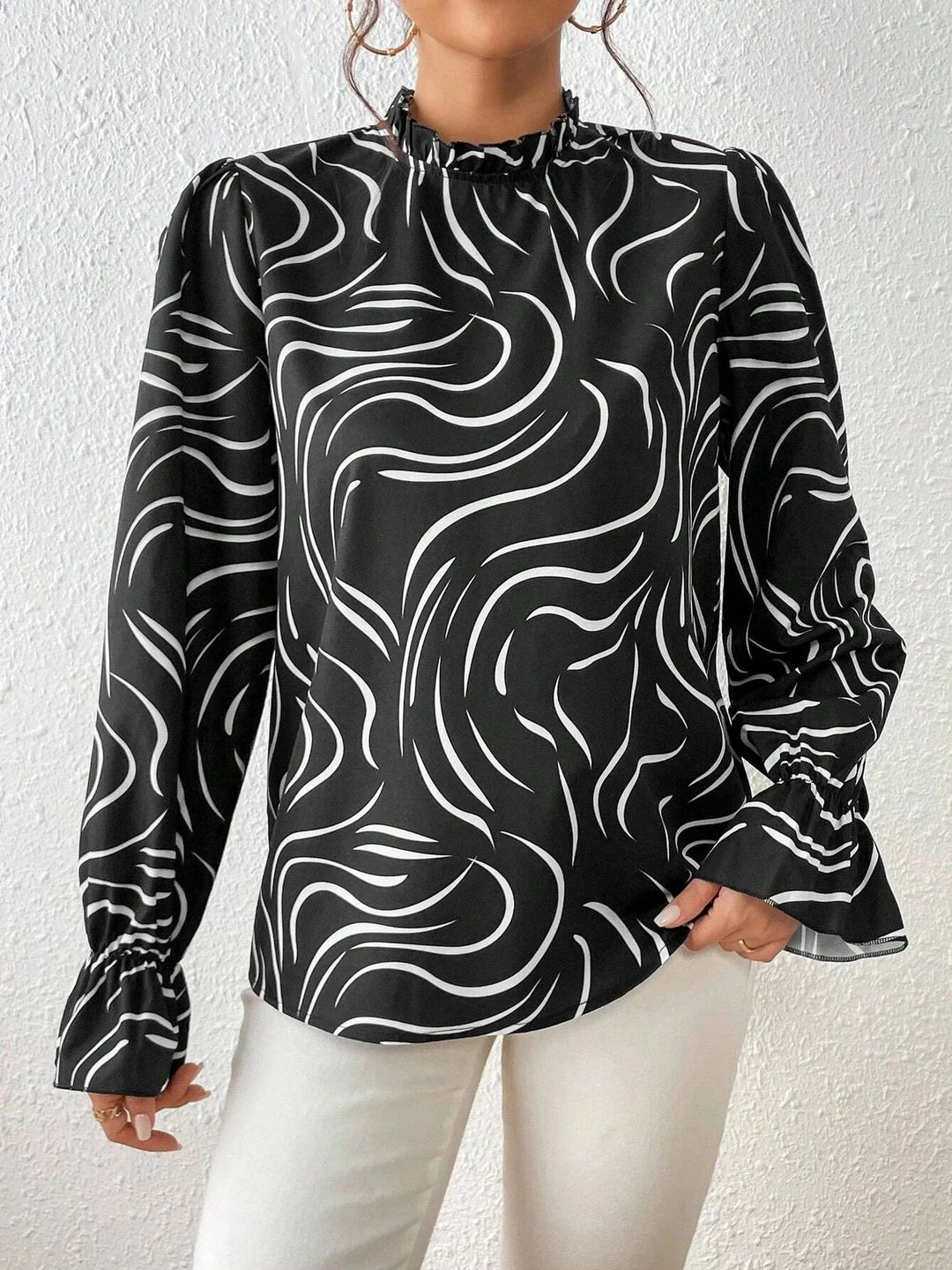 Woman wearing black long sleeve blouse with white abstract swirl pattern and ruffled cuffs