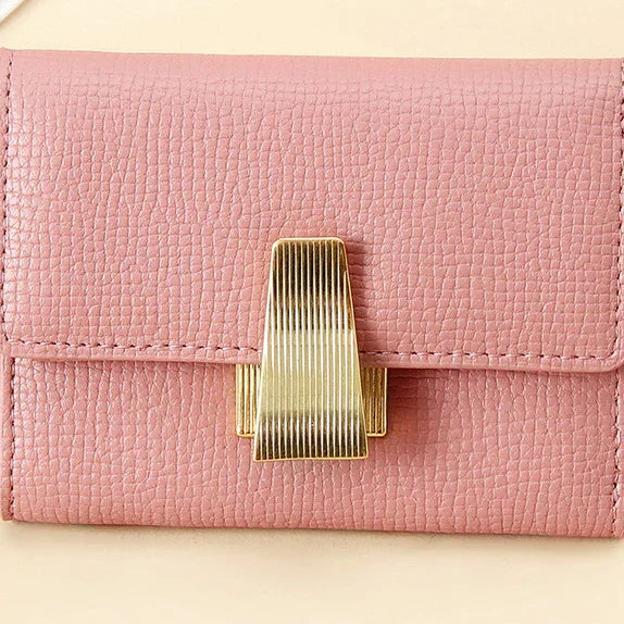 Pink textured leather wallet with a gold striped metal clasp on beige background
