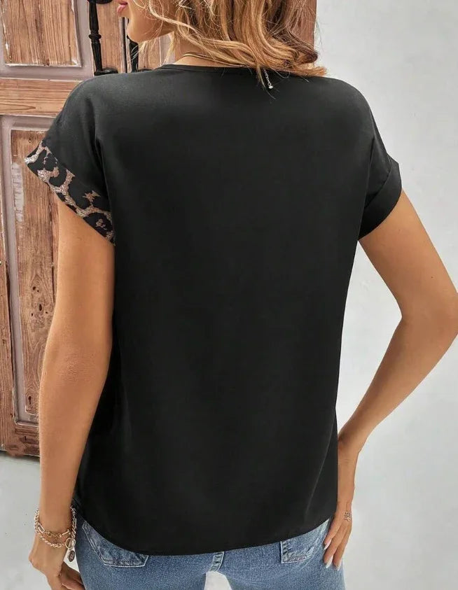 Woman wearing black short-sleeve top with leopard print sleeve cuffs and blue jeans, shown from back