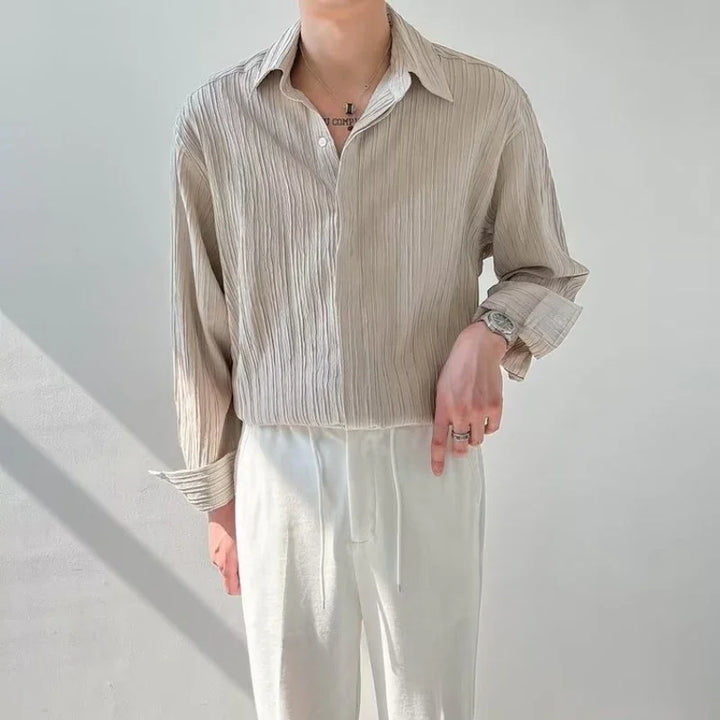 Person wearing beige textured button-up shirt and white pants against plain light background