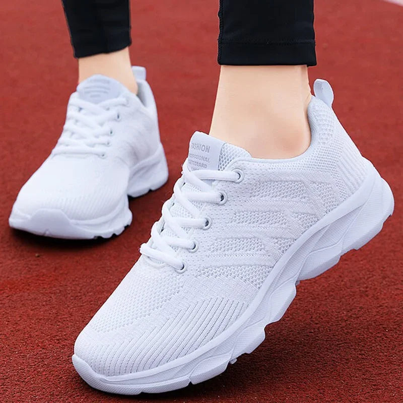 Pair of white lightweight knit sneakers with chunky soles worn on red running track