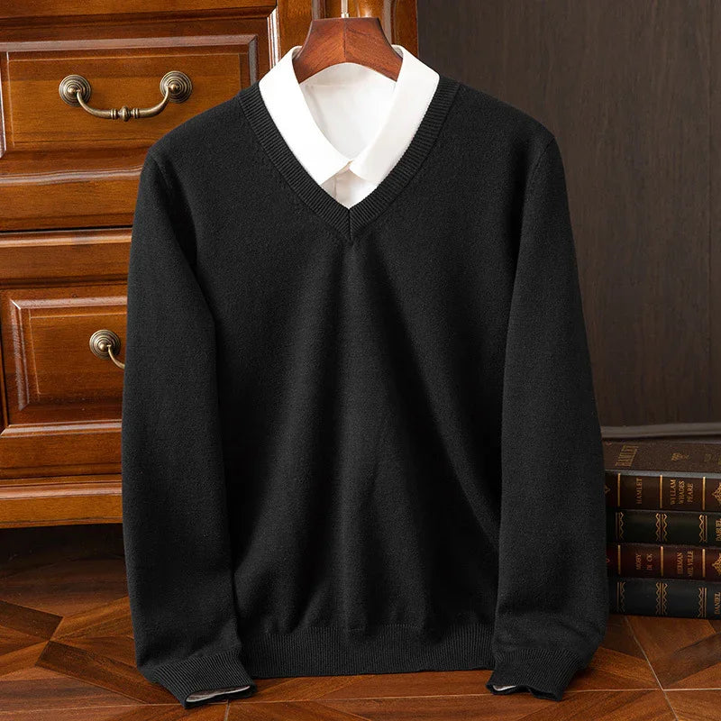 Black V-neck sweater layered over white collared shirt on wooden hanger with chest of drawers and books