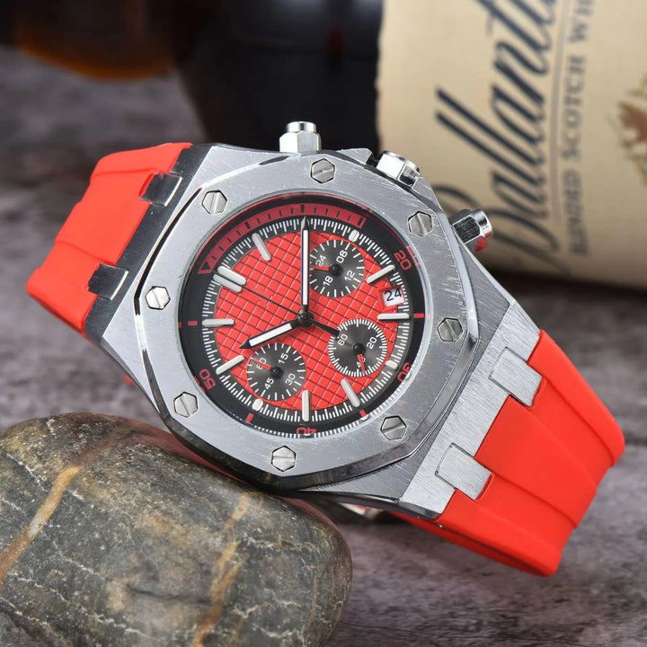 Close-up of stainless steel chronograph watch with red rubber strap on stone surface