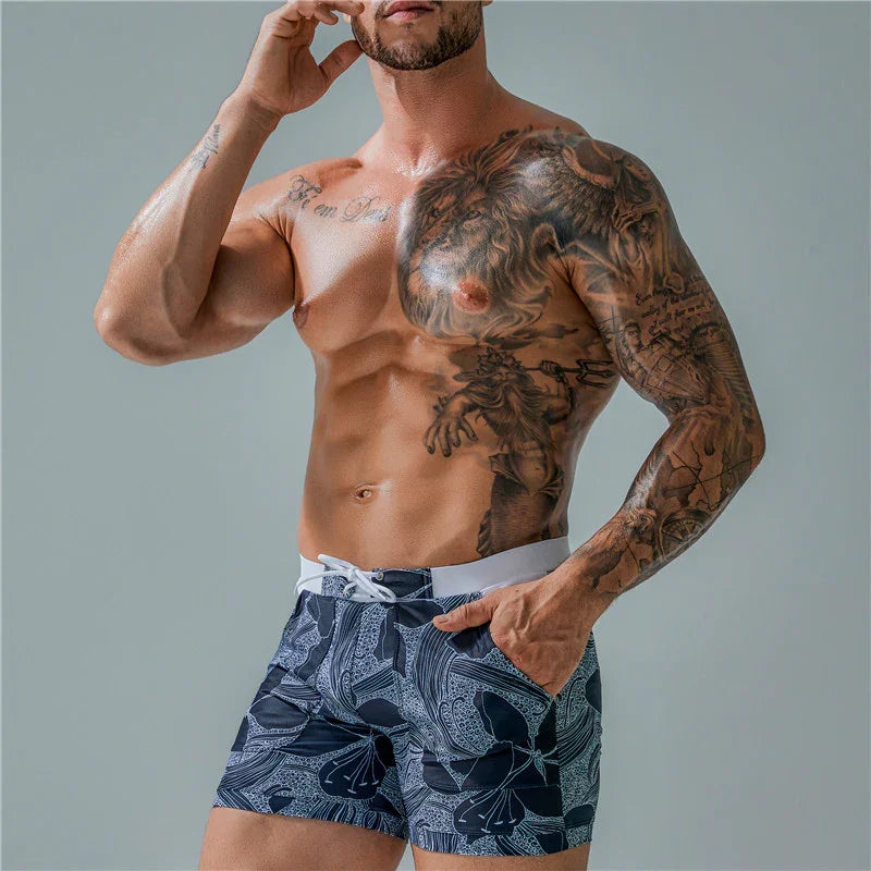 Muscular shirtless man with detailed lion and mythical tattoos wearing navy floral swim shorts