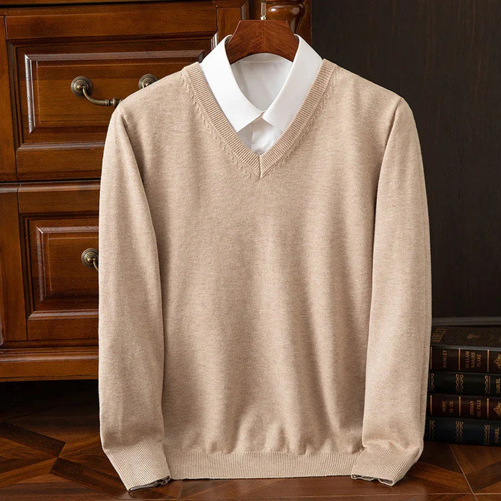 Beige V-neck sweater over white collared shirt displayed on wooden hanger beside vintage wooden drawers and books