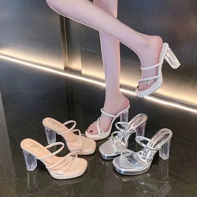 Woman wearing white clear strap high heel sandals with transparent block heels, two pairs of similar shoes on black floor