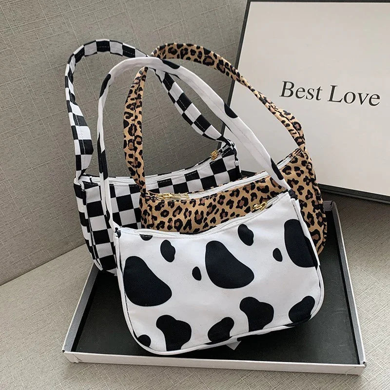 Three small shoulder bags with checkerboard, leopard print, and cow print patterns displayed on a tray with a 'Best Love' sign