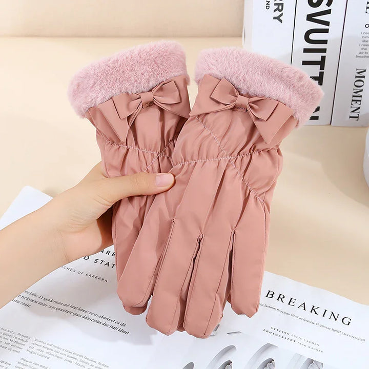 Pink winter gloves with fuzzy cuffs and decorative bows held above magazine pages