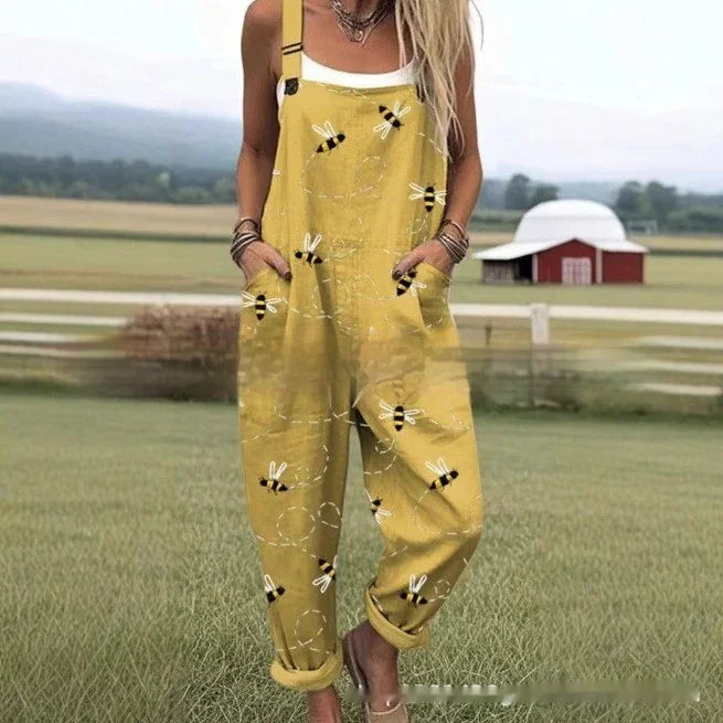 Woman wearing yellow overalls with bee print standing on grassy field with farm buildings in background