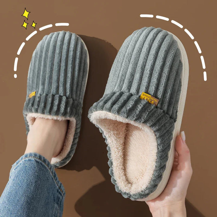 Gray ribbed plush slippers with soft white fleece lining, held by hand and worn on foot