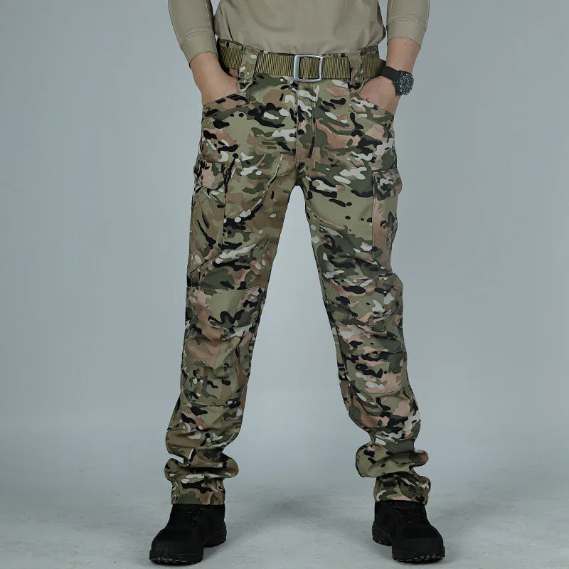Man wearing camouflage tactical cargo pants with a tan belt and black boots on gray background