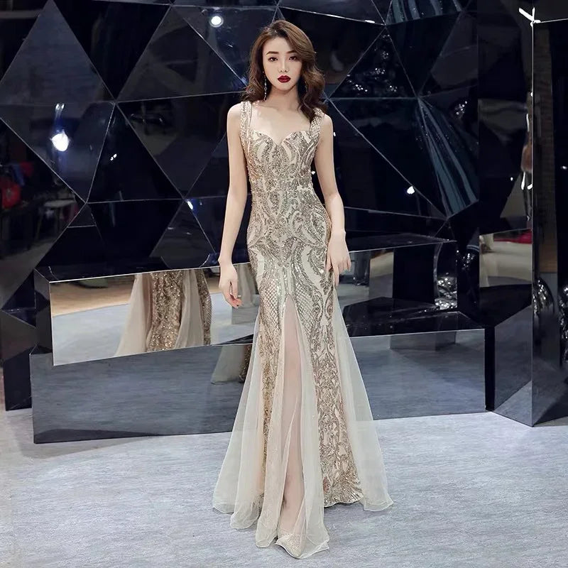 Elegant woman in a gold sequined evening gown with sheer skirt panels posing in a modern black geometric room