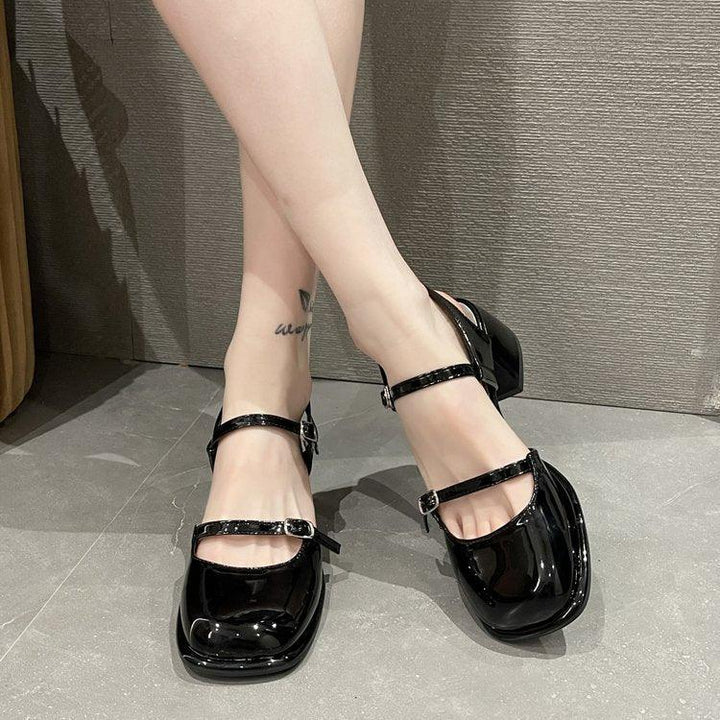 Close-up of legs wearing shiny black Mary Jane style block heel shoes with double straps on gray floor