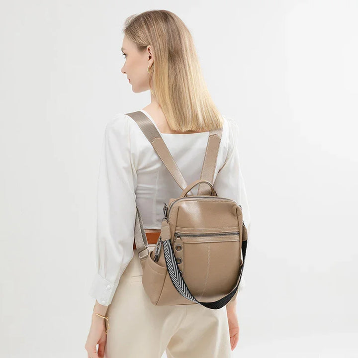 Woman wearing beige leather backpack with zipper and patterned strap on white background