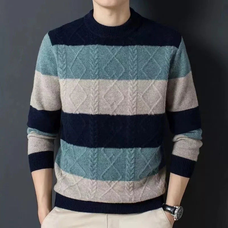 Man wearing a striped cable-knit sweater in blue and beige tones with beige pants against dark background