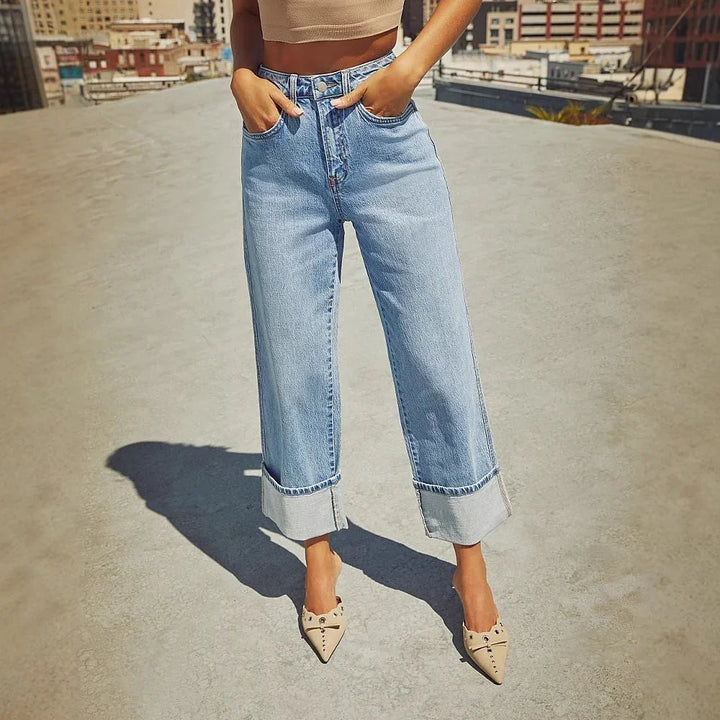 Woman wearing light blue wide-leg cropped jeans with cuffed hems and beige pointed-toe heels on rooftop
