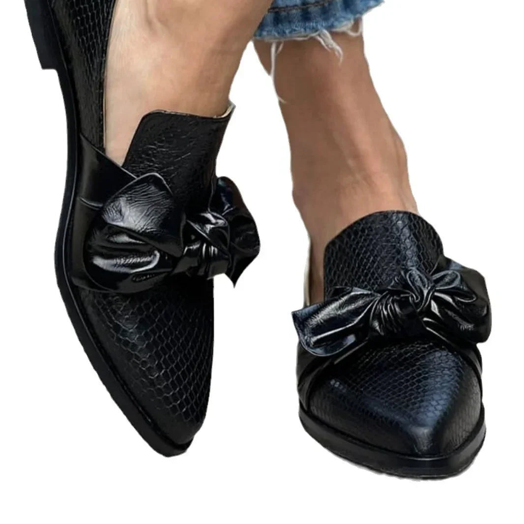 Black crocodile texture pointed loafers with large bow detail worn with frayed hem jeans