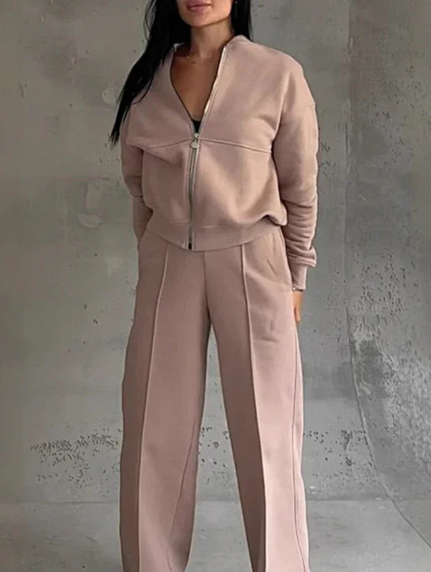 Woman wearing beige zip-up jacket and matching wide-leg pants against a concrete wall