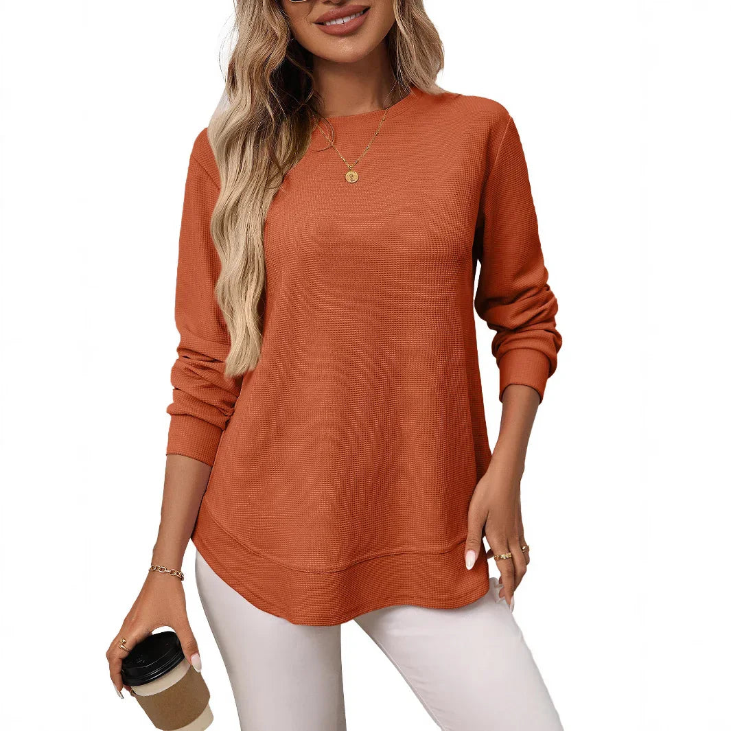 Woman wearing rust orange textured long-sleeve casual top with white pants holding coffee cup