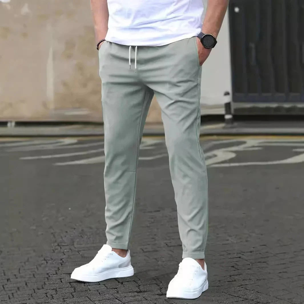 Man wearing light gray jogger pants with white drawstrings and white sneakers standing on asphalt