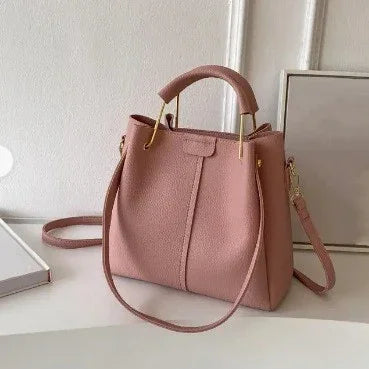 Pink leather handbag with top handle and shoulder strap on white surface near wall and framed art