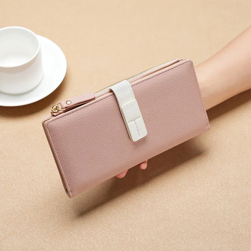 Hand holding a pink leather wallet with a white strap and gold zipper on beige surface