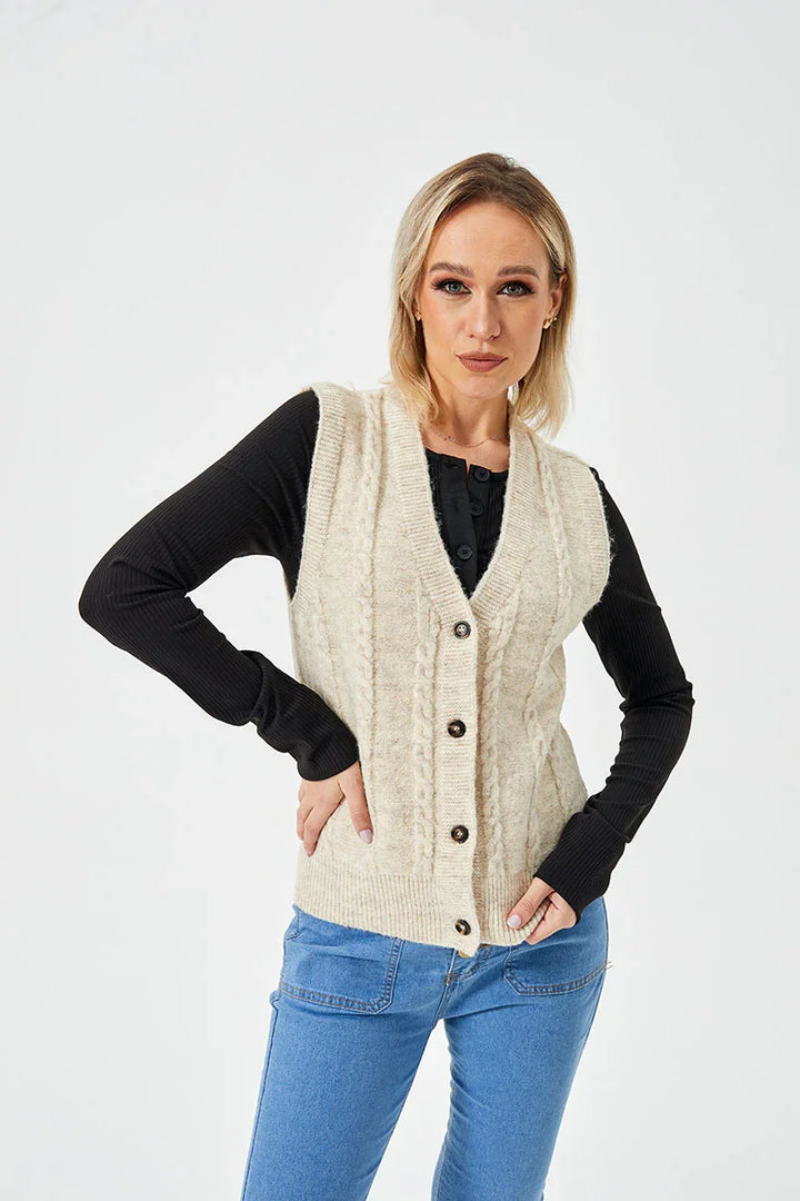 Woman wearing beige cable knit buttoned vest over black long sleeve top and blue jeans