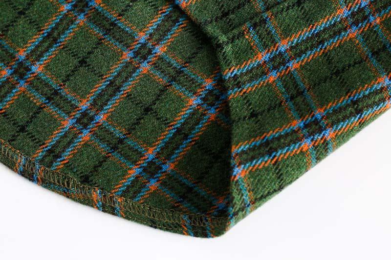 Close-up of green wool fabric with blue and orange tartan plaid pattern on white background
